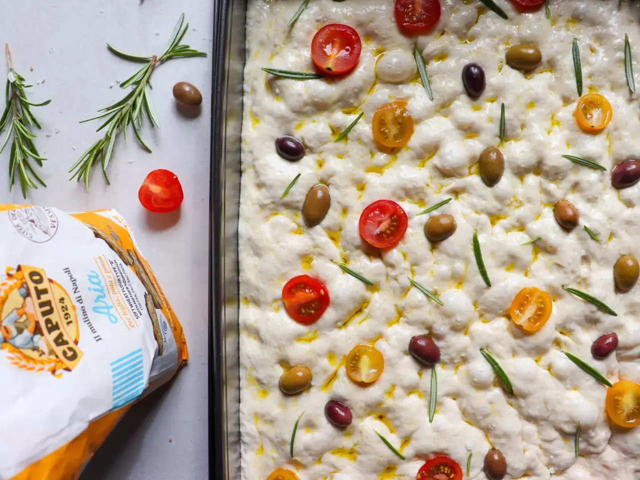 focaccia mit Olivenöl, rosmarin, tomaten und Oliven vor dem backen 