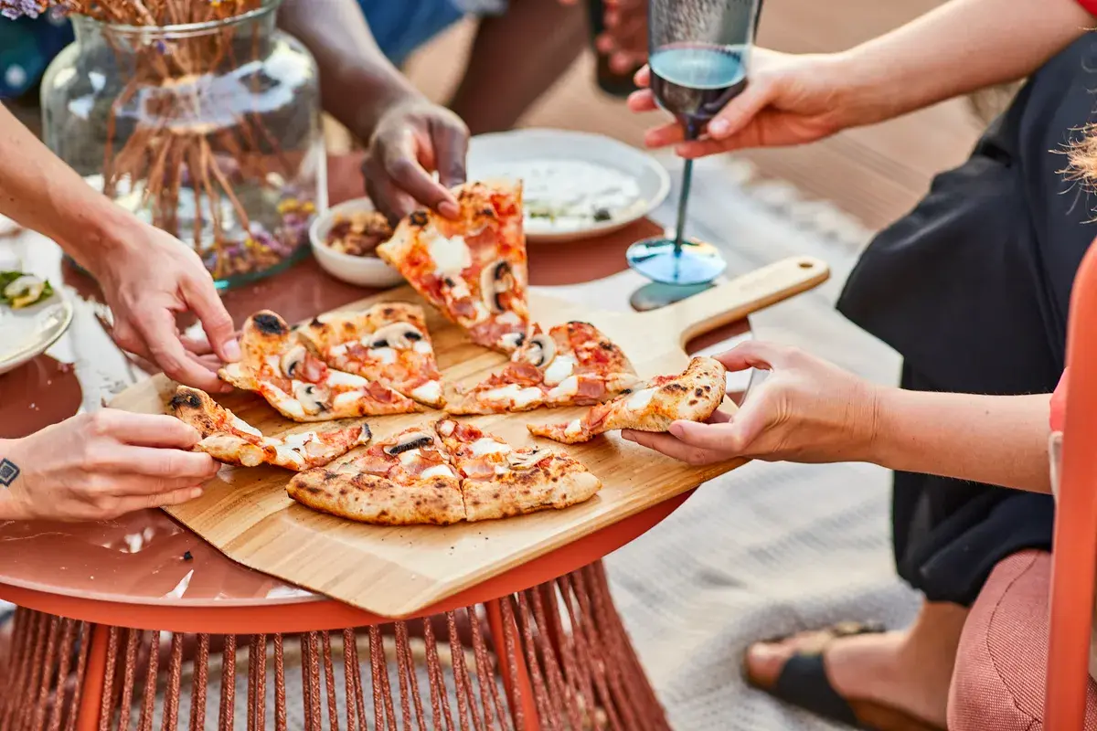 outdoor pizza party setting mit pizzaofen, fertig gebackener pizza und italienischem wein