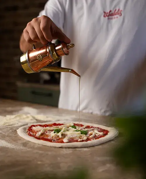 Waldi träufelt Olivenöl über die Pizza