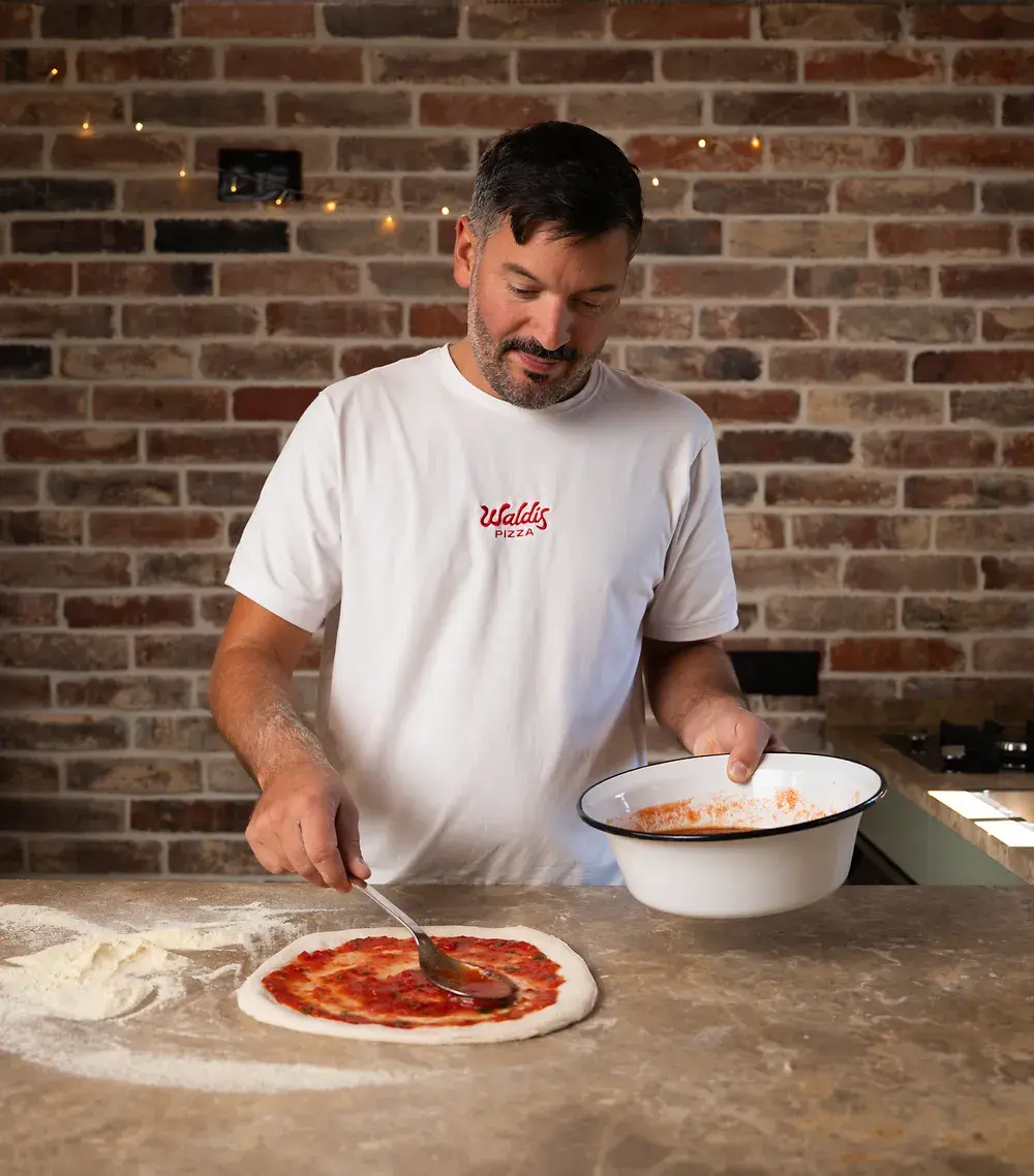 Waldi verbreitet Tomatensoße auf Pizzateig