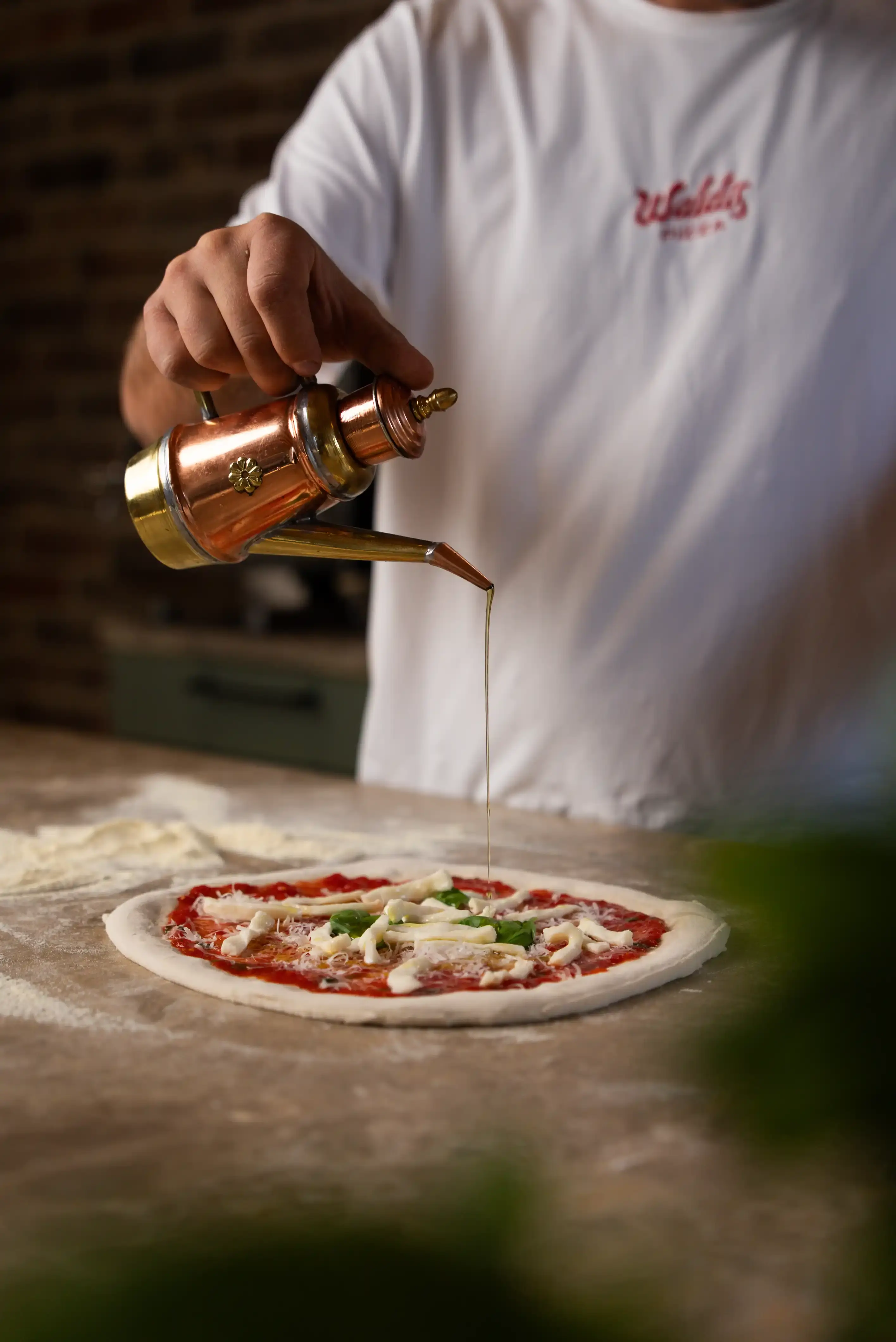 Olivenöl in Kanne auf belegte Pizza gießen