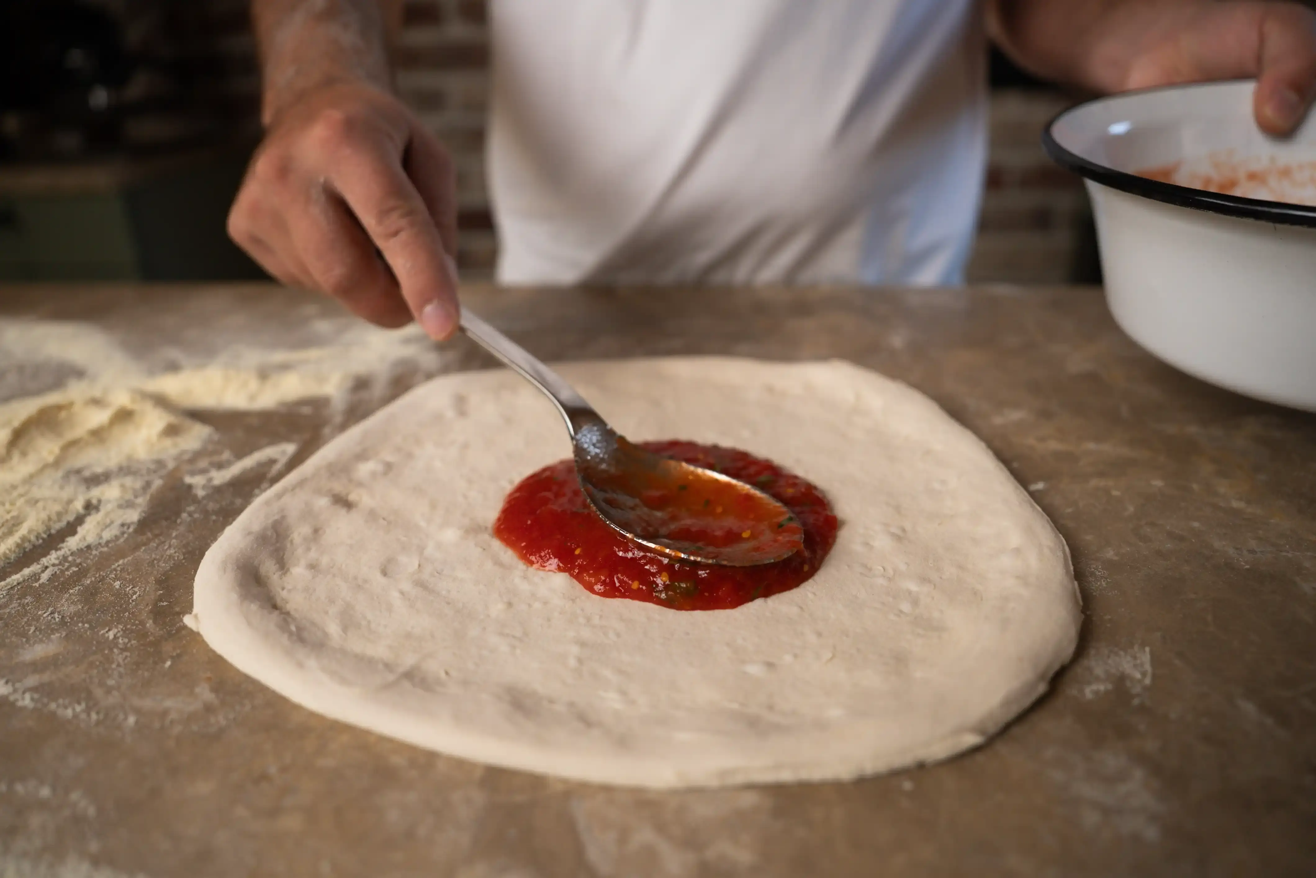 Tomatensouce auf den ausgebreiteten Pizzaboden verteilen