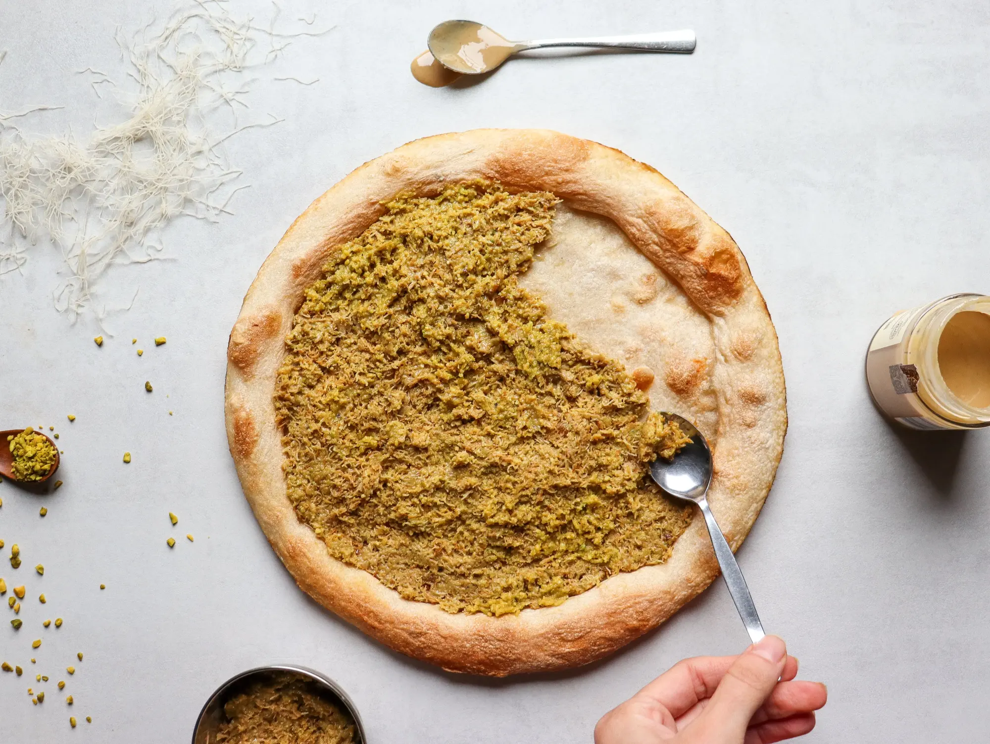 Pistaziencreme wird auf den gebackenen Pizzaboden gestrichen