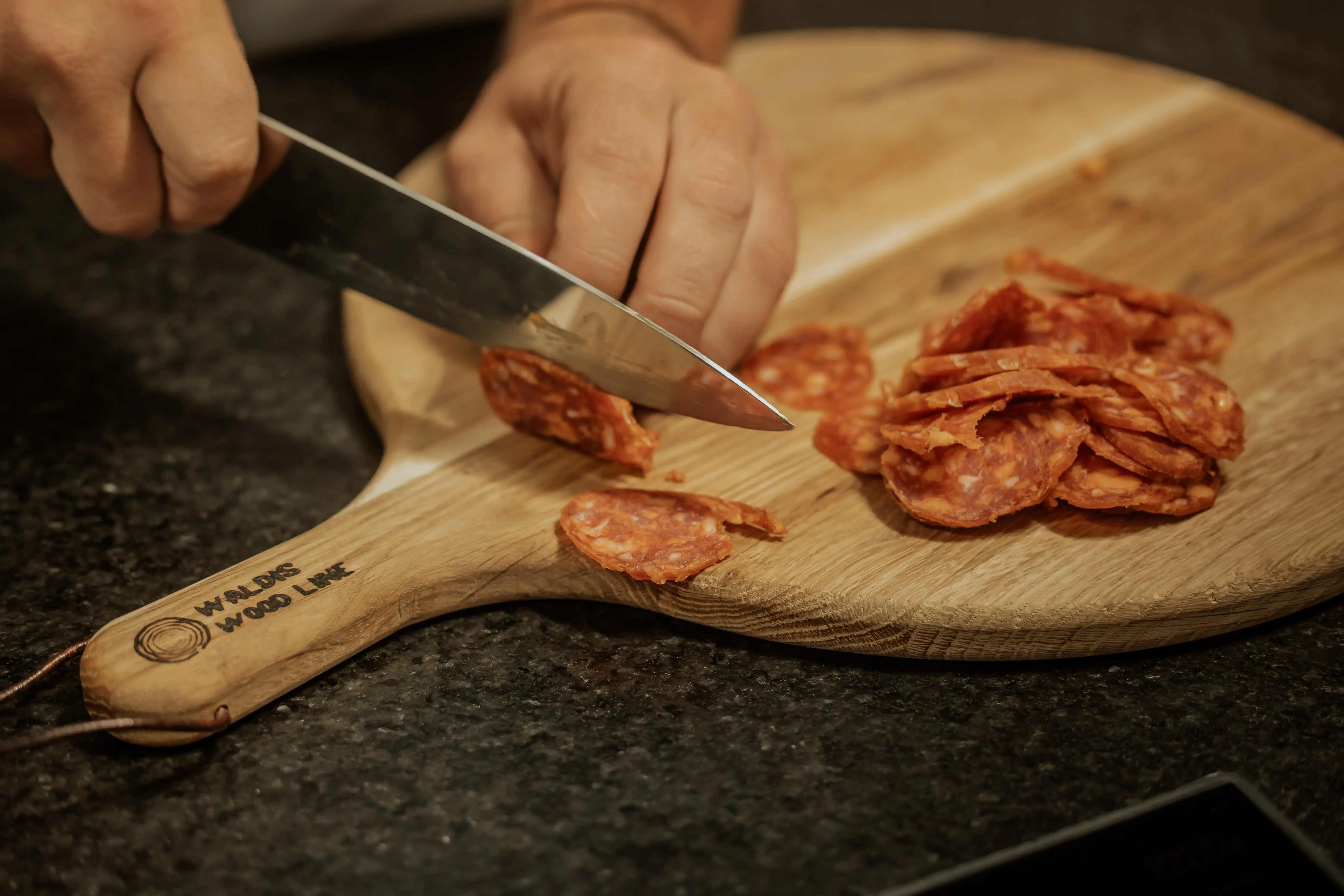 Scharfe Salami wird auf dem Holzbrett in Scheiben geschnitten