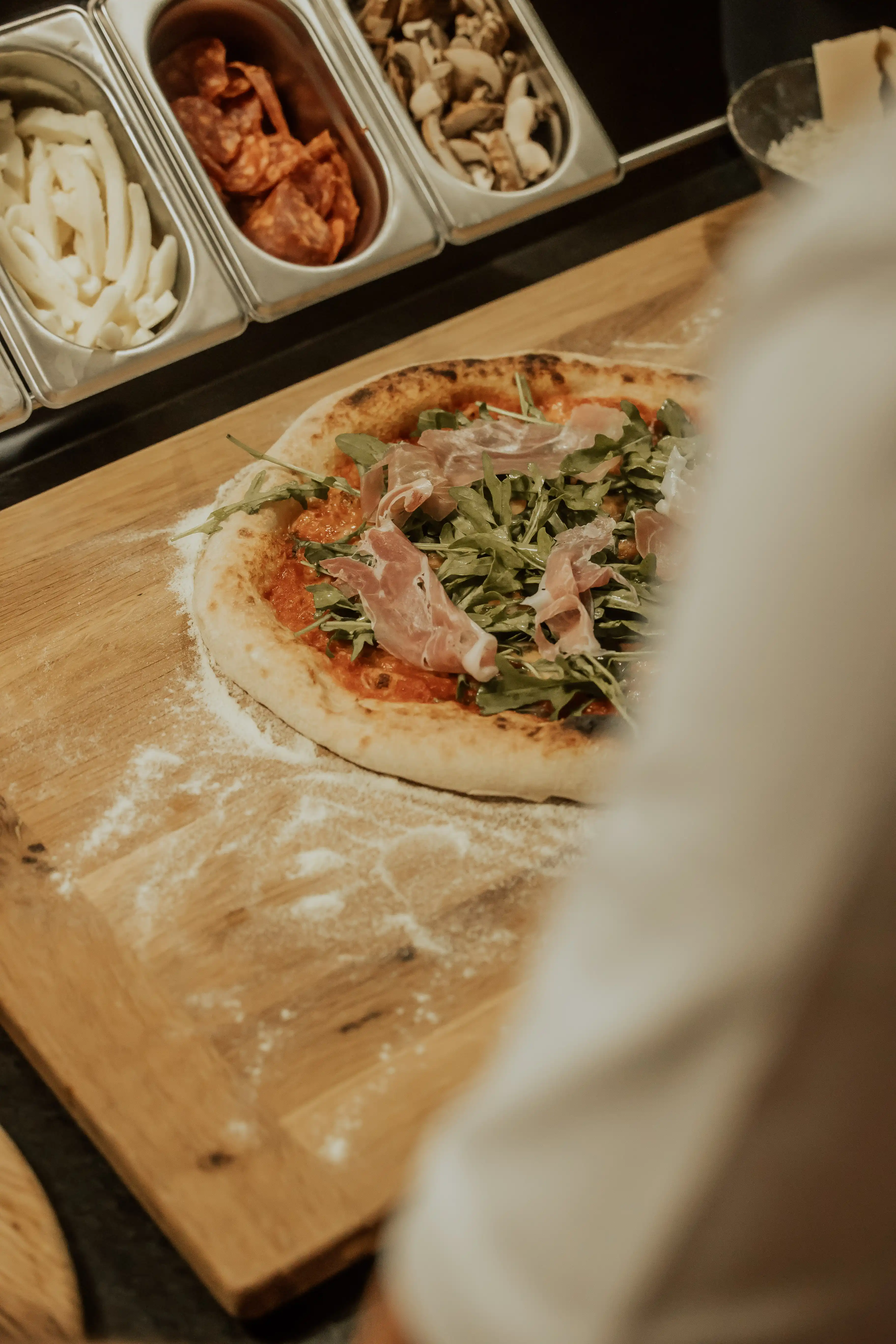 Aceto Balsamico di Modena IGP von Giusti wird in einem feinen Faden über eine Pizza mit Prosciutto, Rucola und Käse geträufelt