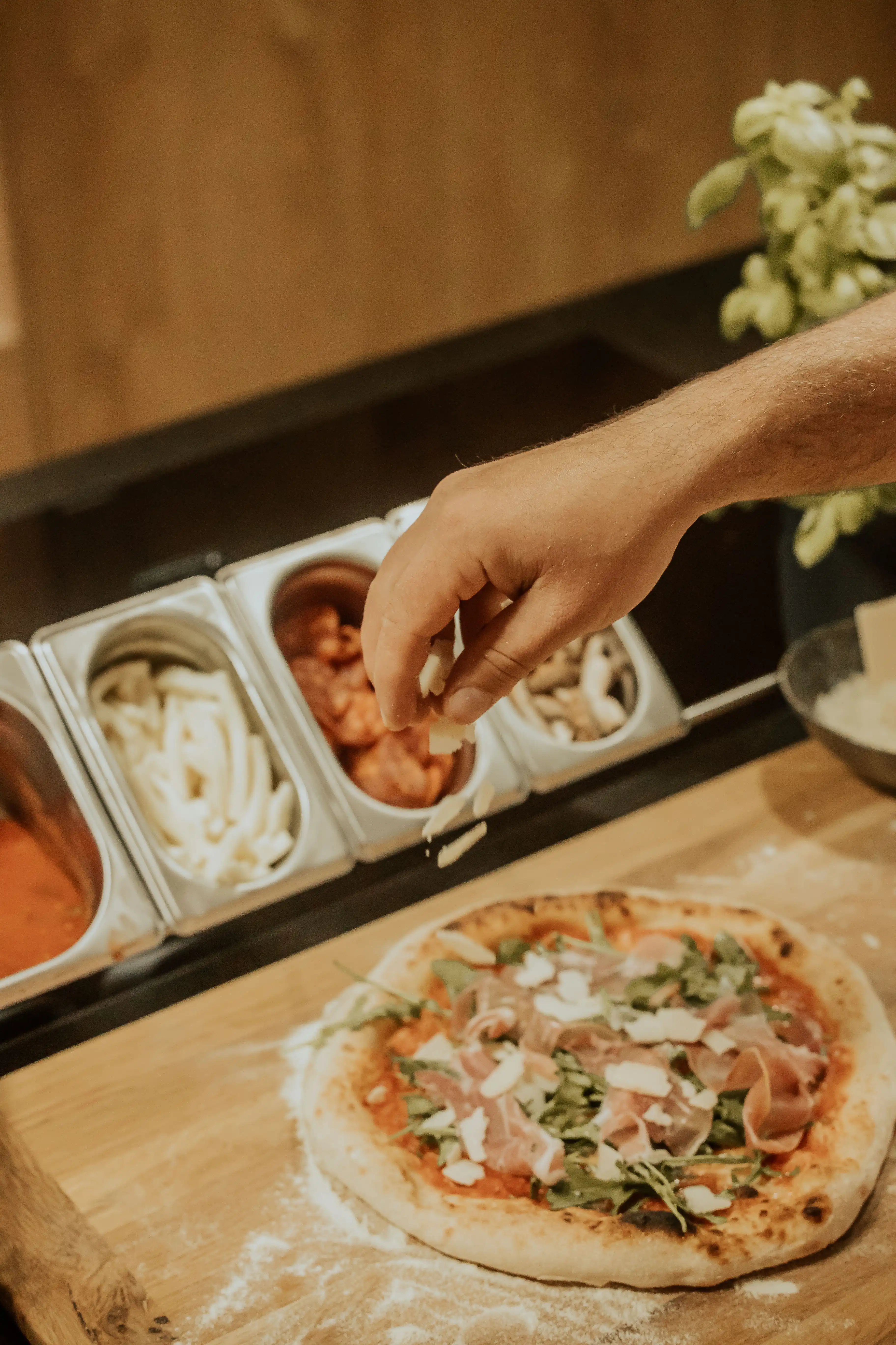 Gehobelter Käse wird nach dem Backen über eine Pizza mit Prosciutto crudo und Rucola gestreut
