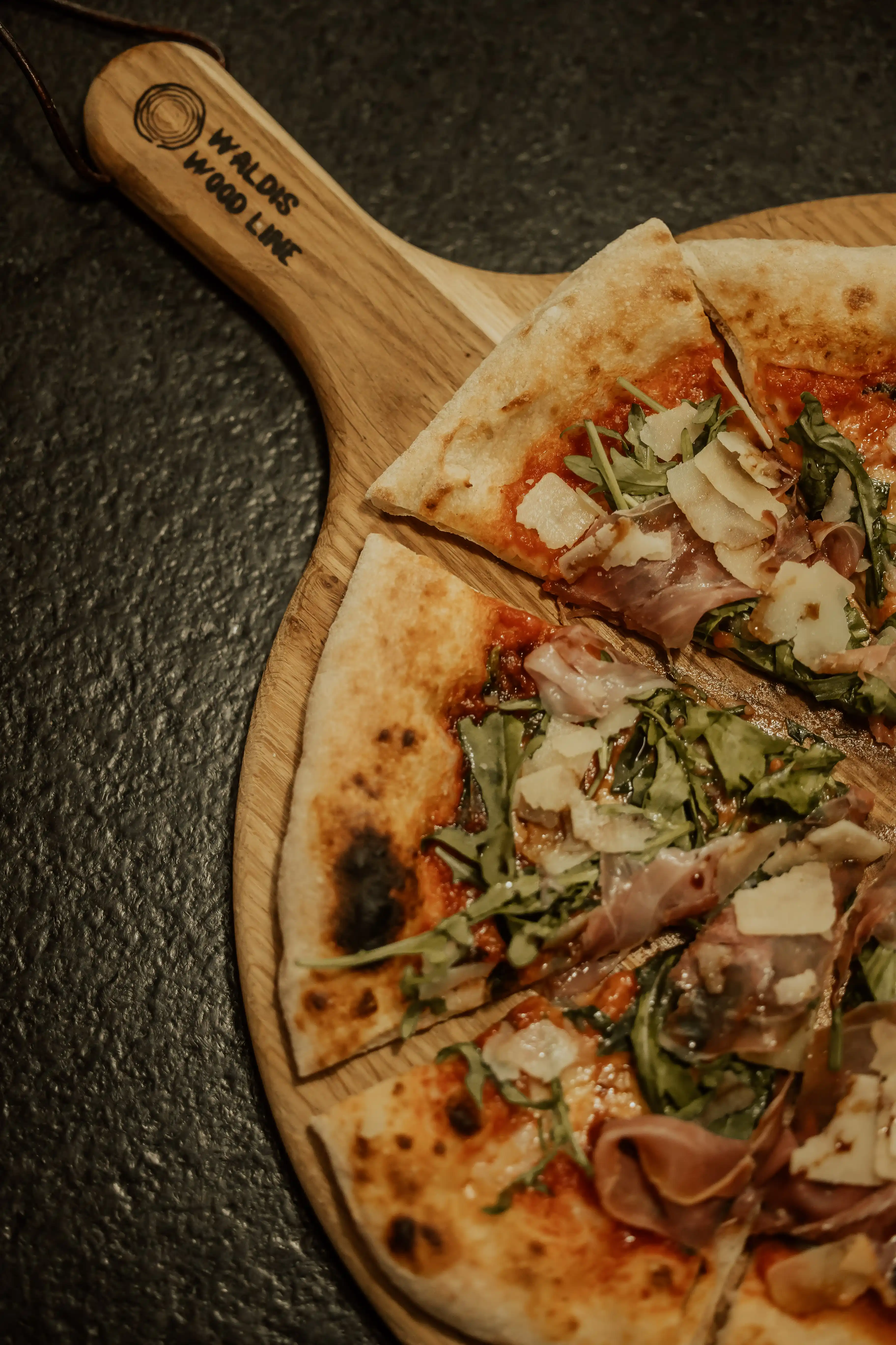 Gebackene Pizza Margherita wird mit Rucola belegt, daneben ein Stück Hartkäse und frisches Basilikum